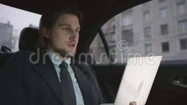 一个英俊的男人，棕色头发，穿着开心果衬衫，灰色西装，坐在车里，在笔记本上工作